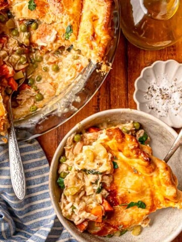 Chicken pot pie with a serving scooped out and a bowl of pie beside it on a wooden table.