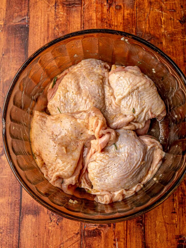 Raw chicken thighs coated in garlic rosemary marinade in a glass bowl, ready to rest before baking.