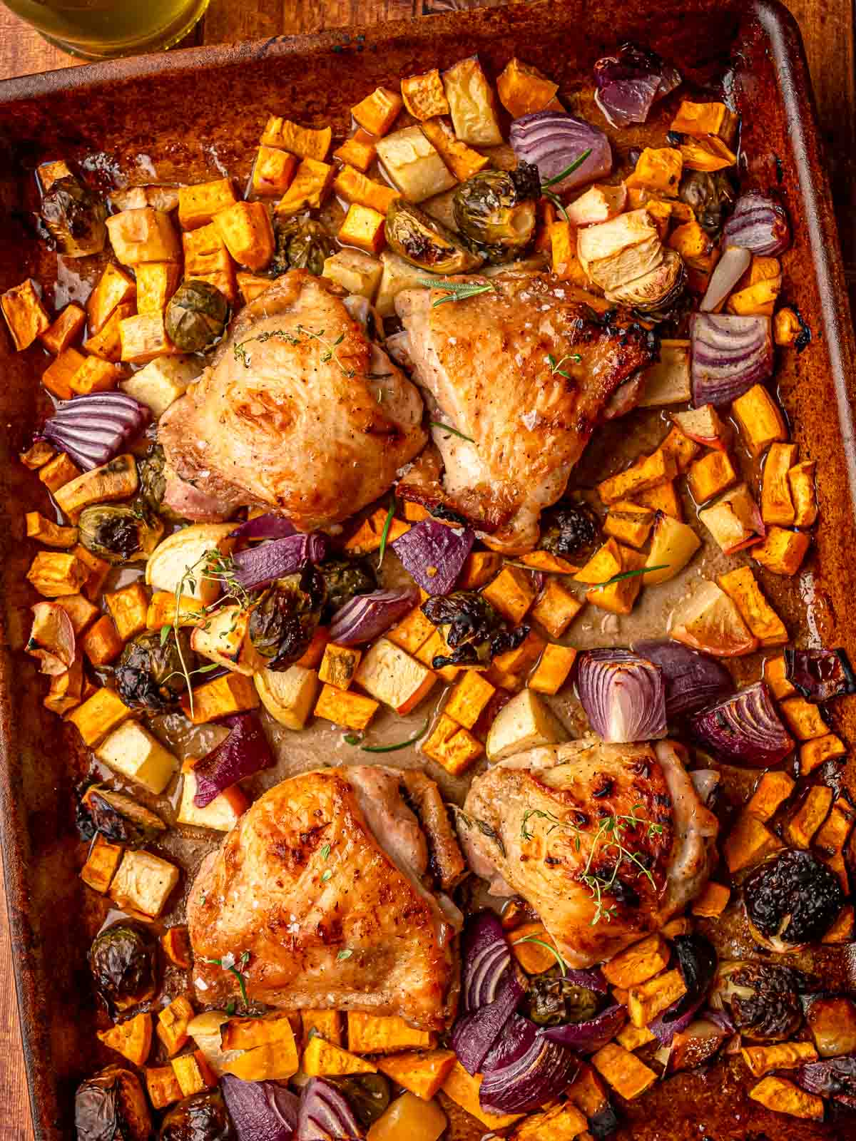 Close view of the finished garlic rosemary chicken and vegetables on a baking sheet, garnished with thyme and ready to serve.