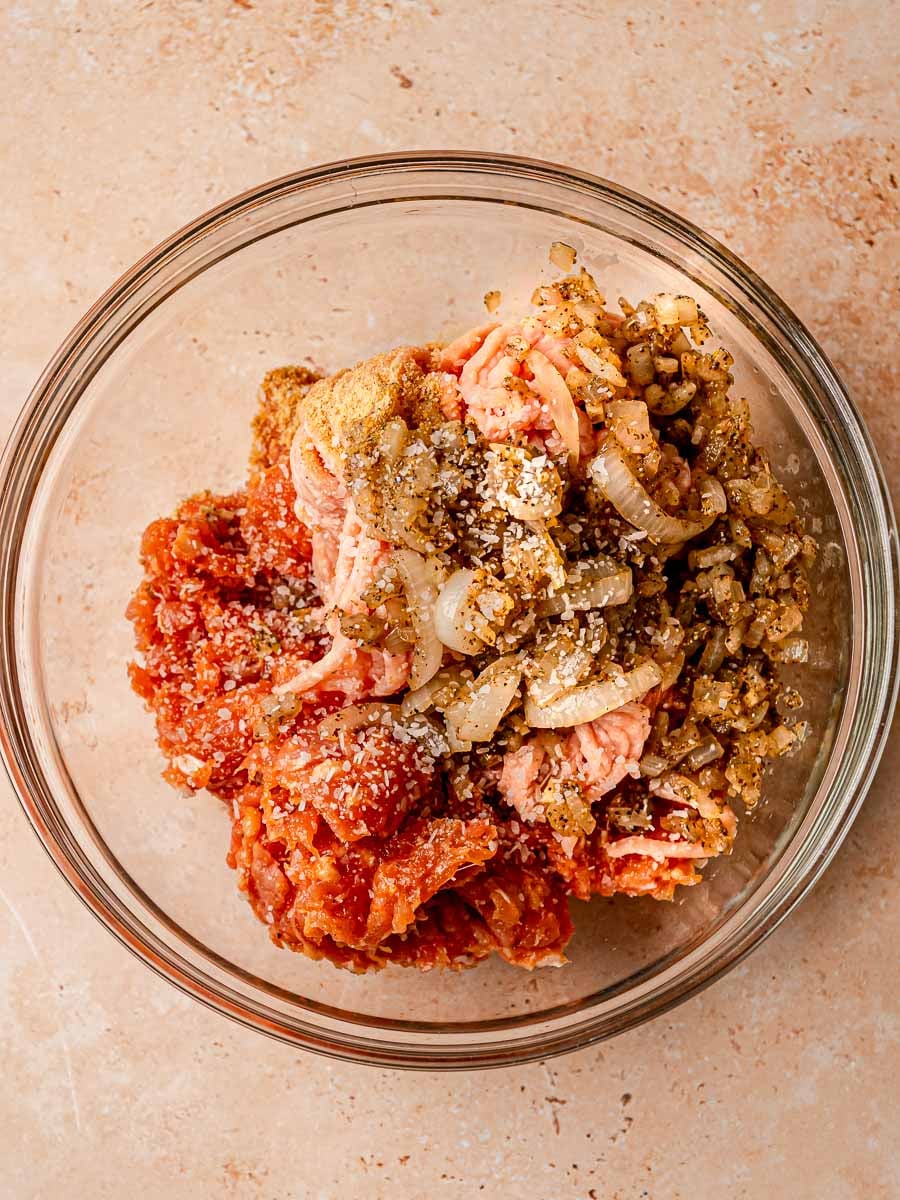 Ground chicken, cooked onions, and seasonings in a glass mixing bowl.