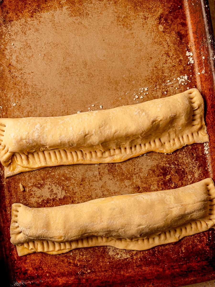 Two long unbaked chicken sausage rolls sealed in puff pastry on a sheet pan.