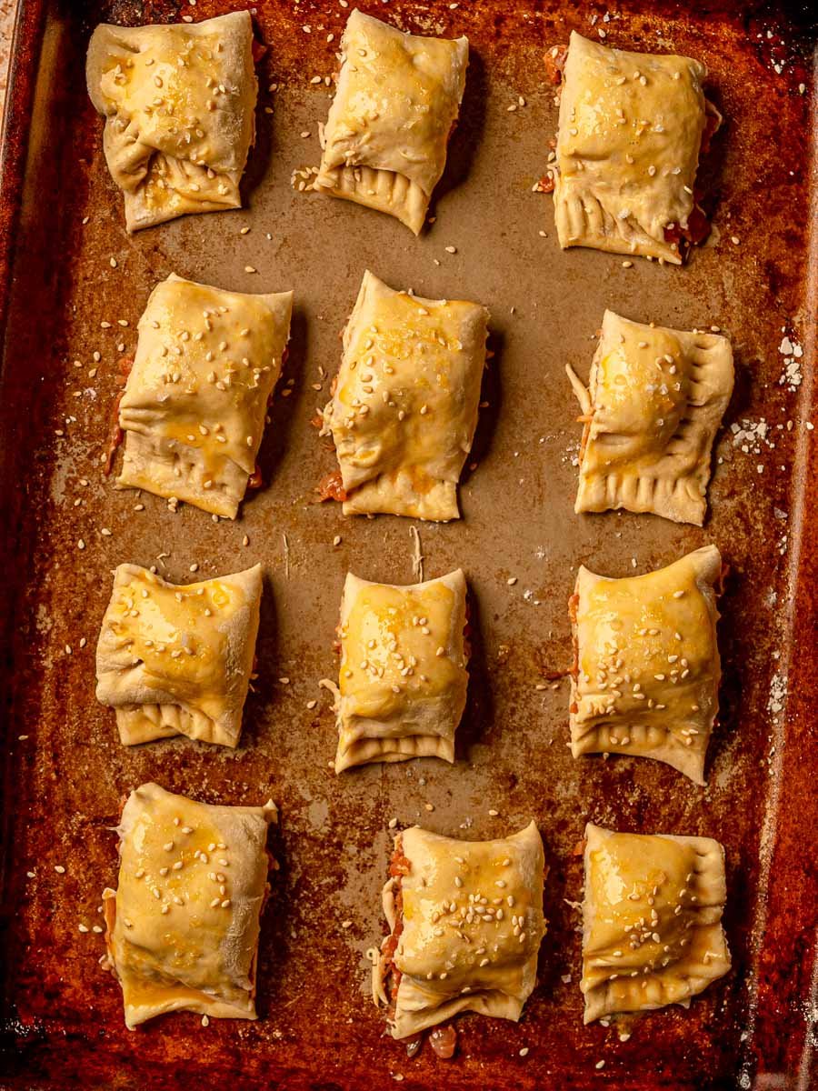 Cut chicken sausage rolls on a baking sheet brushed with egg wash and sprinkled with sesame seeds.