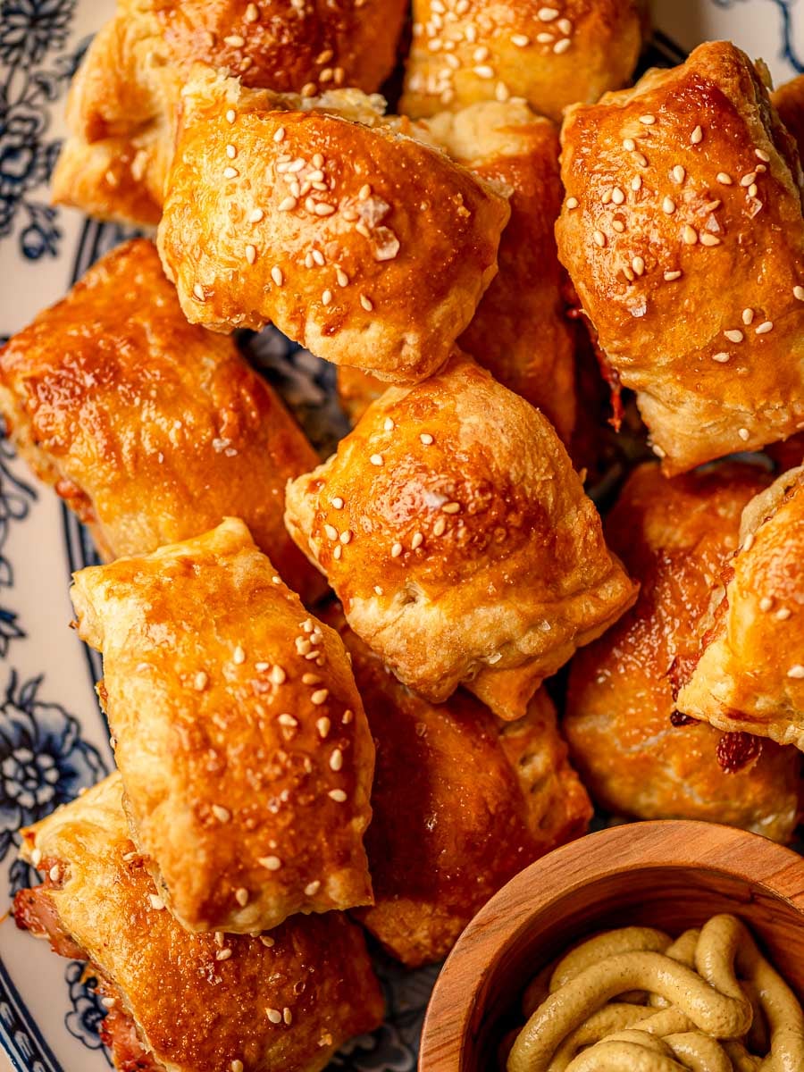 Baked chicken sausage rolls piled on a platter with sesame seeds and flaky salt on top.