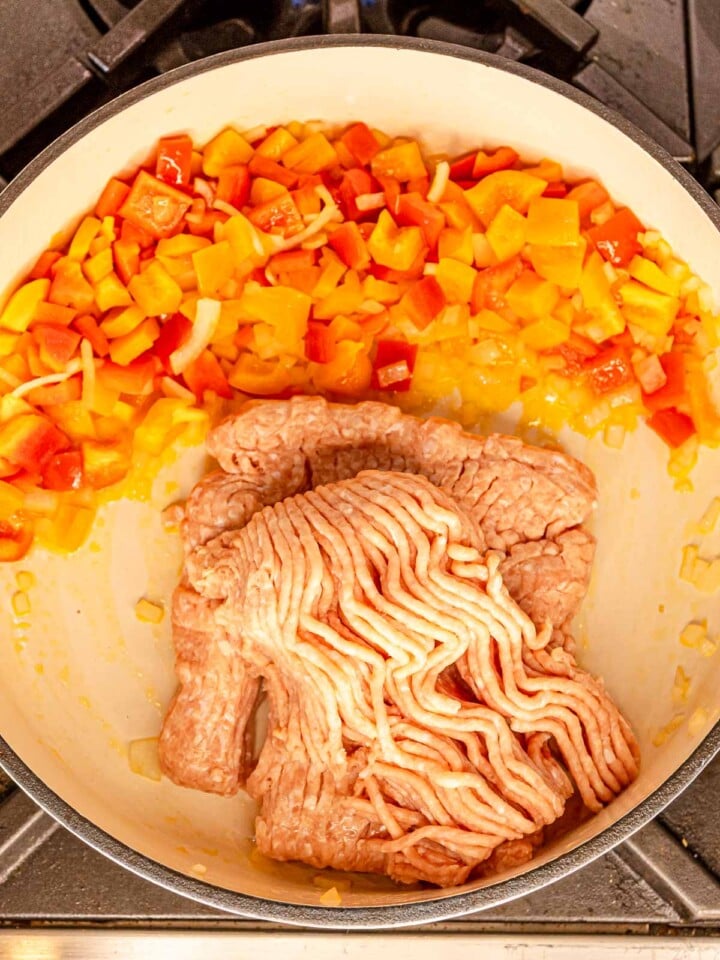 Ground chicken added to one side of the skillet with sautéed bell peppers and onions.