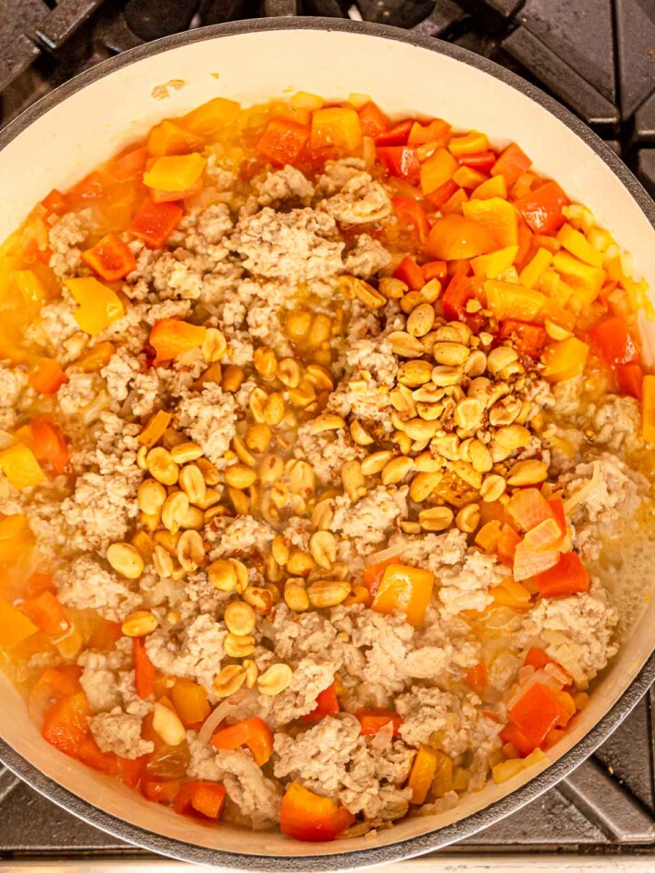 Cooked ground chicken and bell peppers simmering with peanuts in the skillet.