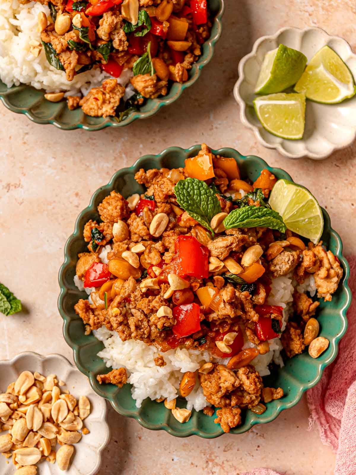 Ground chicken stir fry served over white rice in green bowls with lime wedges on the side.