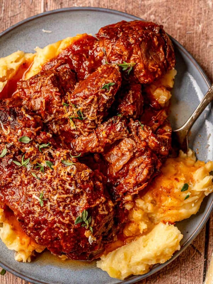 Italian pot roast with mashed potatoes, tomato and red wine gravy, and fresh thyme on a plate.