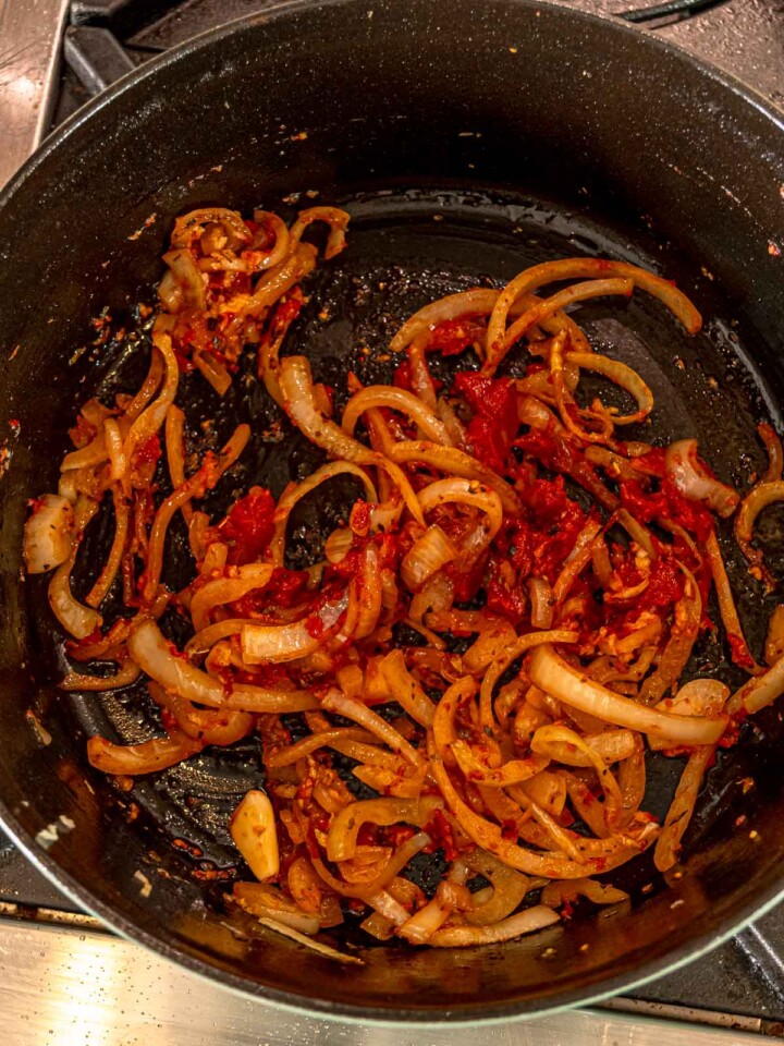 Sliced onions, garlic, and tomato paste sautéing in the bottom of a Dutch oven.