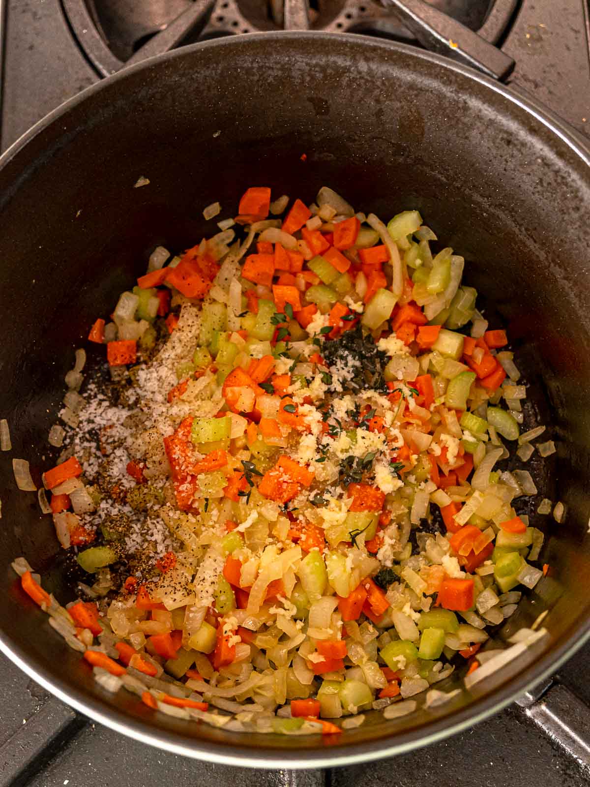Sautéed vegetables in a pot topped with garlic, herbs, salt, and pepper.