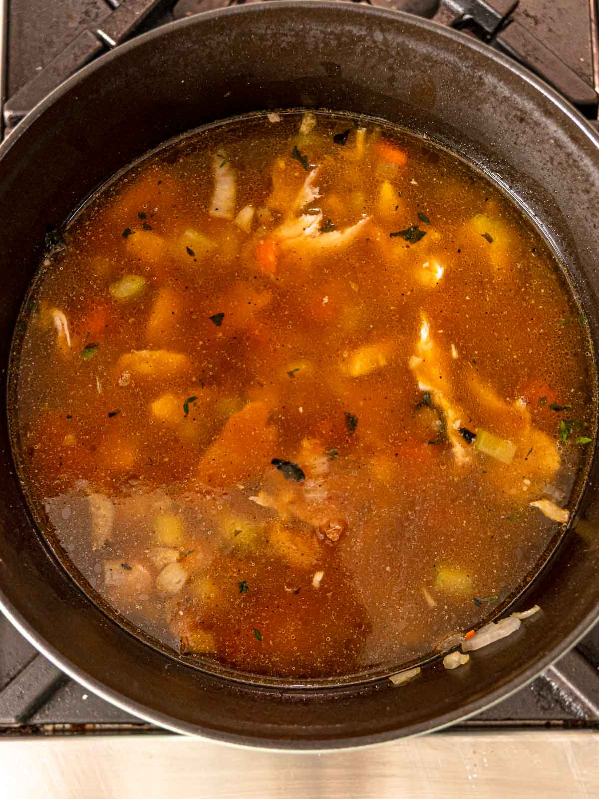 Dutch oven with turkey broth, vegetables, and shredded turkey simmering for soup.