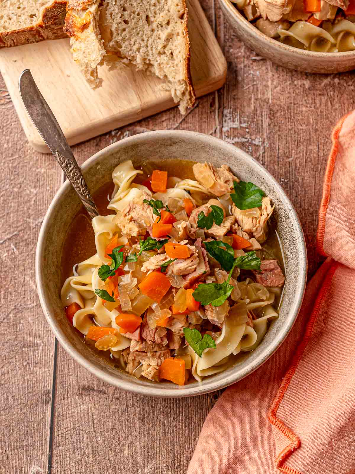 Bowl of turkey noodle soup with noodles, vegetables, and bread on the side.