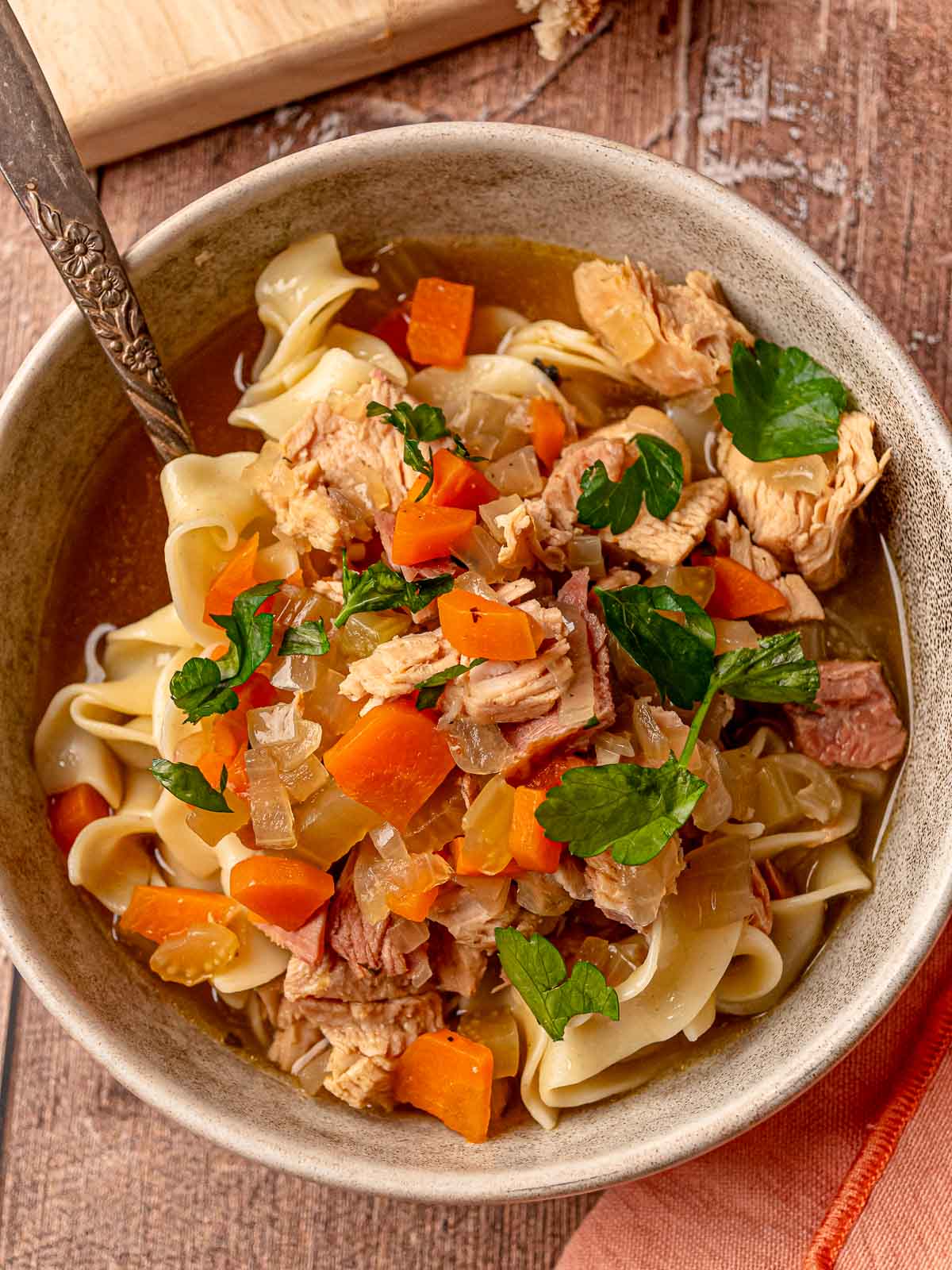 Leftover turkey noodle soup in a bowl garnished with parsley, showing noodles and veggies.