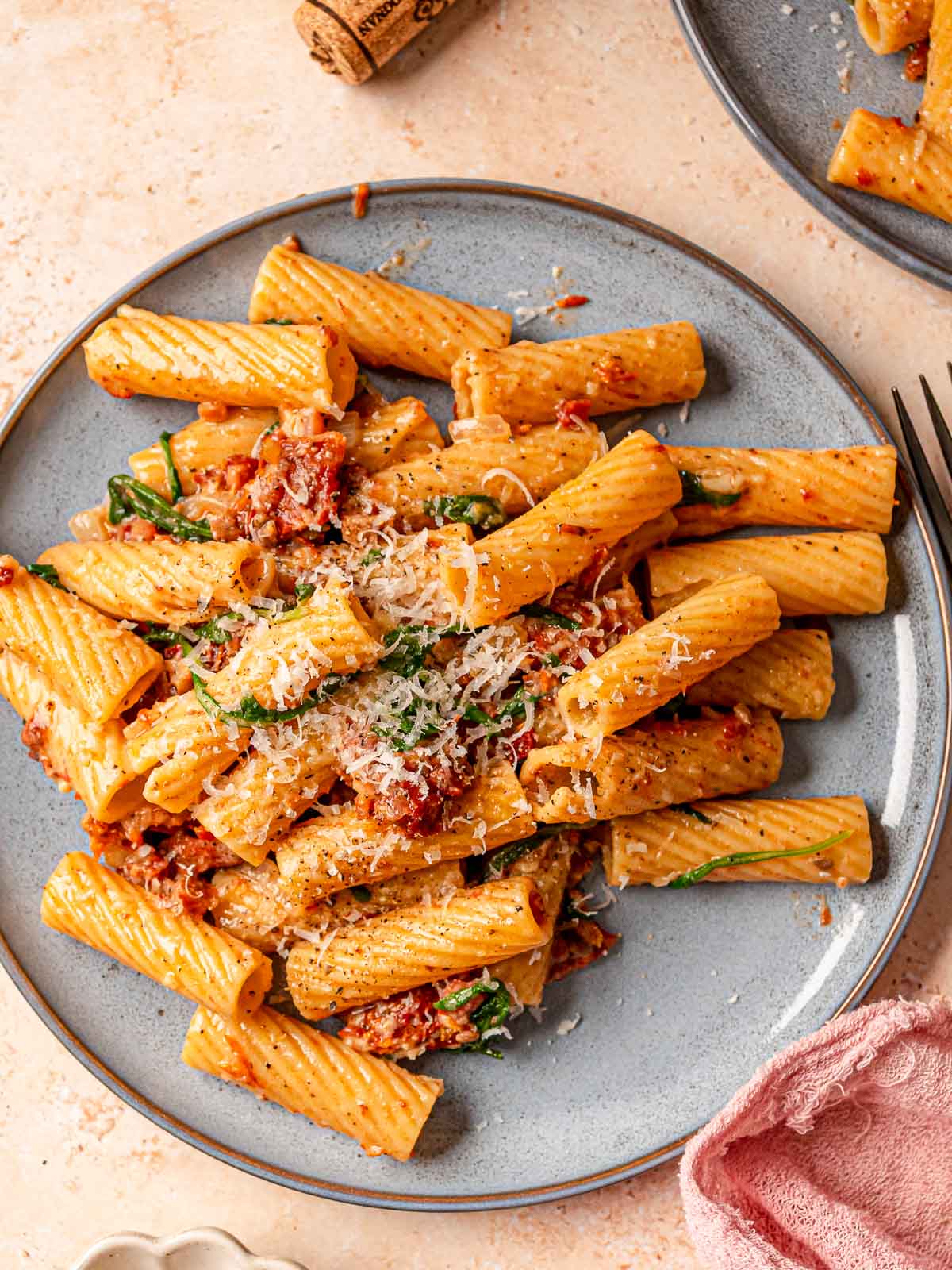 Plate of sun-dried tomato rigatoni with pancetta, greens, and Parmesan cheese.