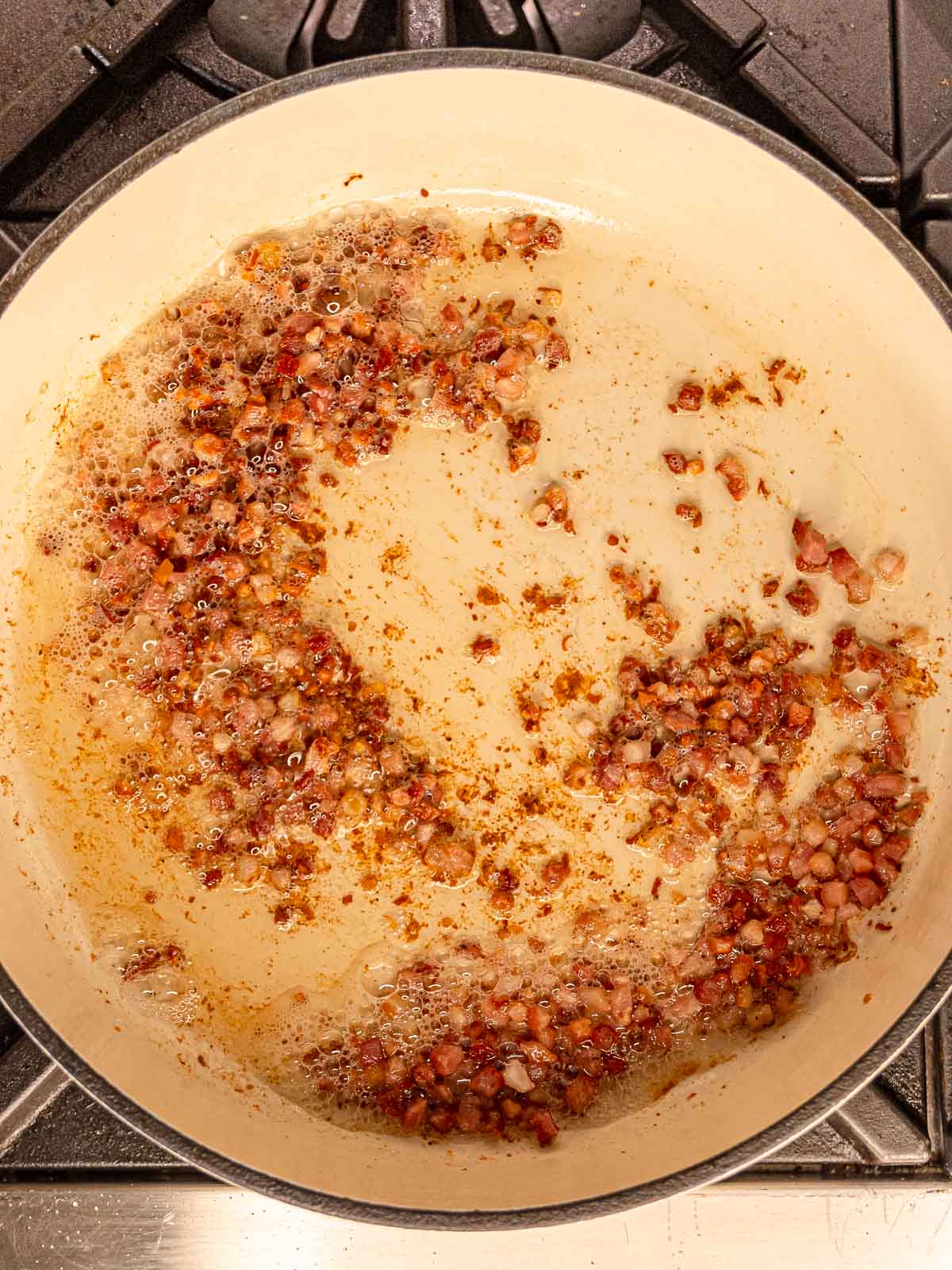 Diced pancetta sizzling in a skillet with rendered fat and browned bits.