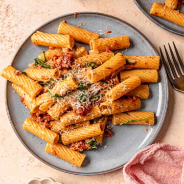A blue plate of rigatoni with cream sauce, pancetta and sun-dried tomatoes.