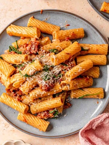 A blue plate of rigatoni with cream sauce, pancetta and sun-dried tomatoes.