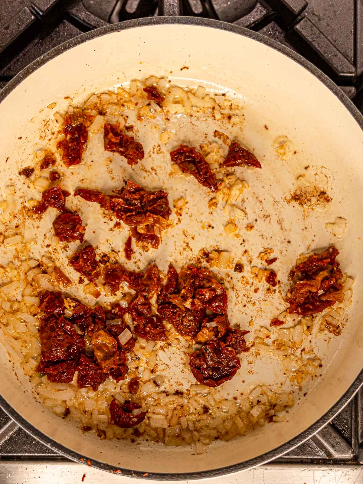 Chopped onions, garlic, and sun-dried tomatoes sautéing in a skillet.