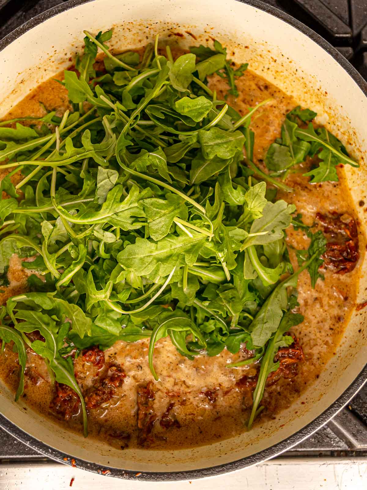 Fresh arugula added to the skillet of sun-dried tomato cream sauce.