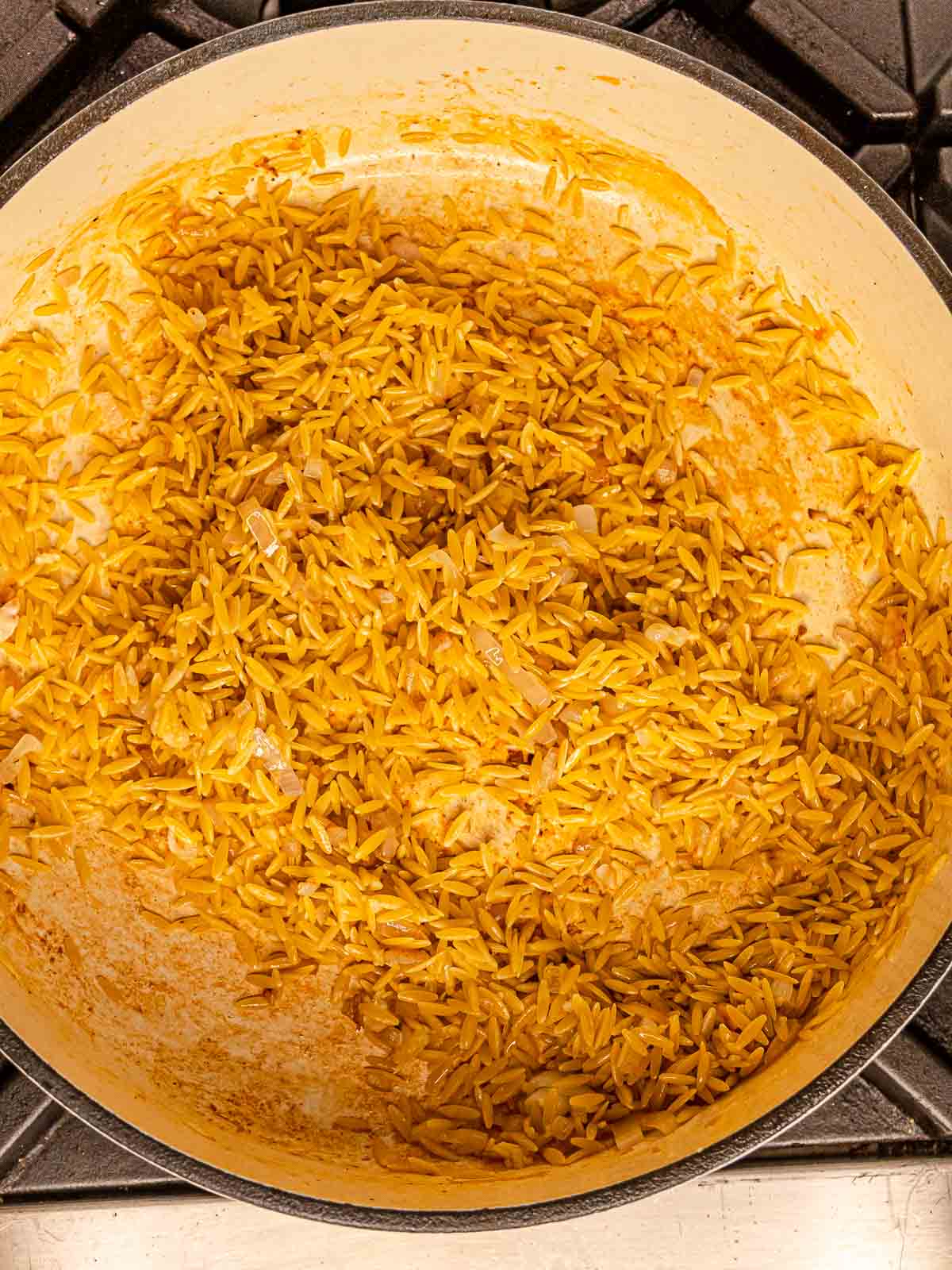 Dry orzo pasta stirring in a pot with sautéed shallots.