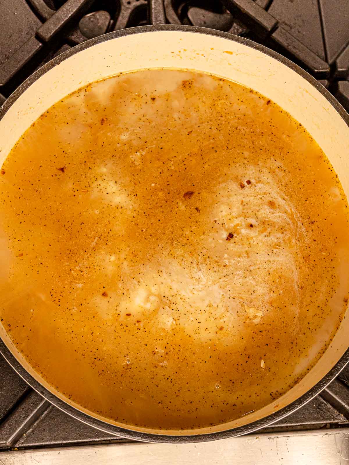 Chicken broth simmering in a pot over orzo and aromatics.