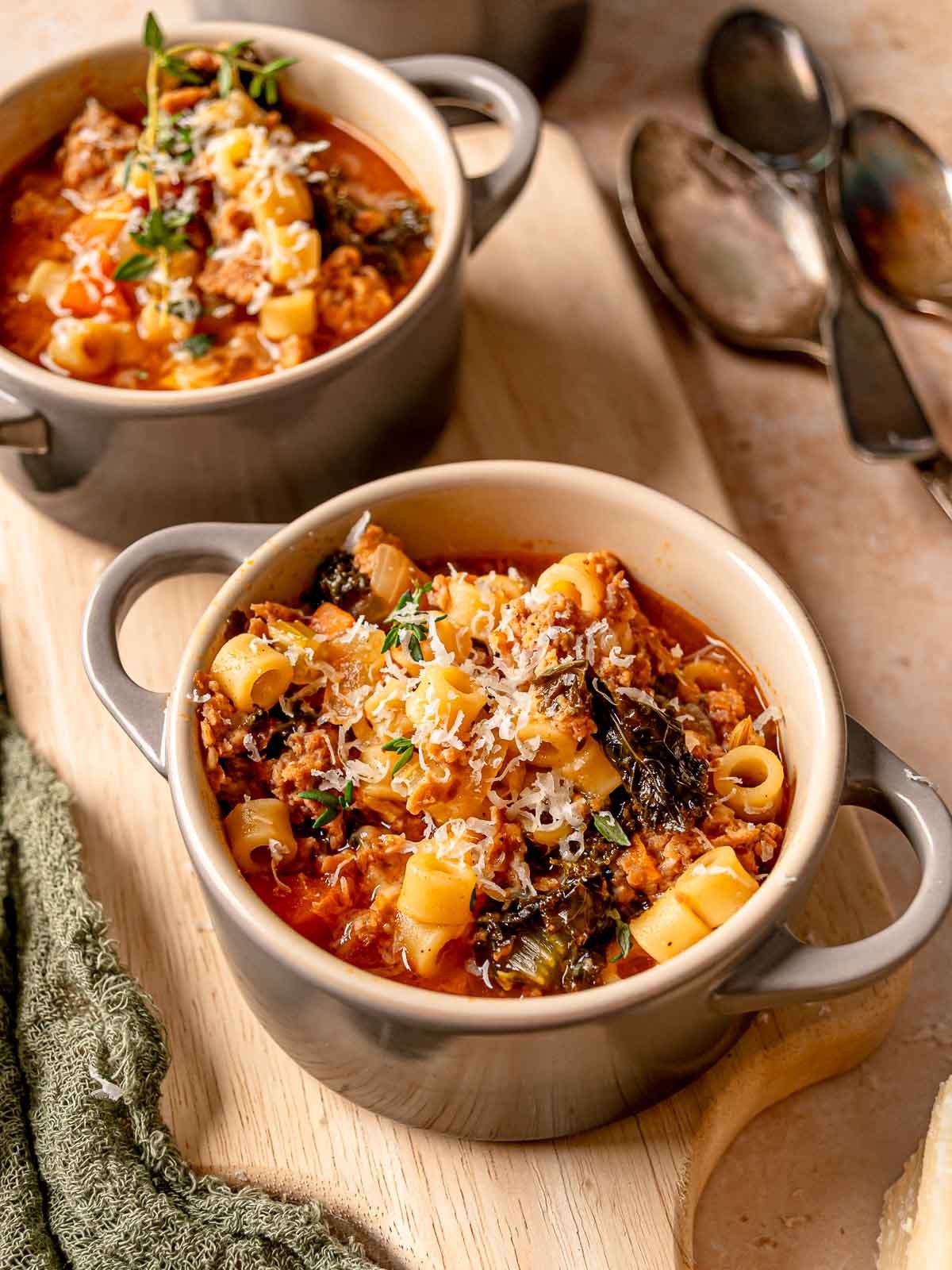 Italian sausage kale soup served in a ceramic bowl with ditalini, grated cheese, and thyme.