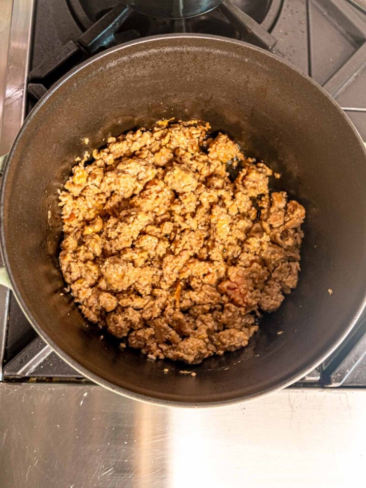 Ground Italian sausage browning in a Dutch oven with rendered juices.