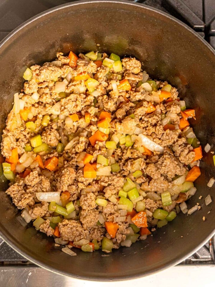 Italian sausage simmering with diced onion, celery, and carrots.