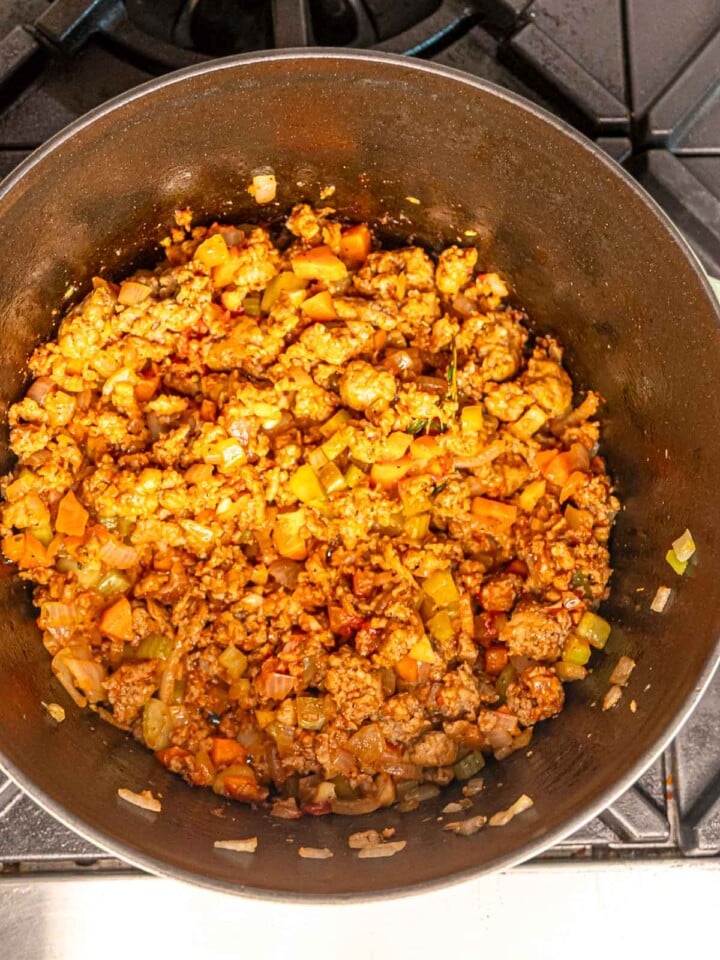 Sausage mixture coated in tomato paste and herbs as it cooks with vegetables.
