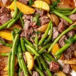 Sheet pan steak bites with roasted potatoes, green beans, garlic-butter sauce, and fresh parsley.
