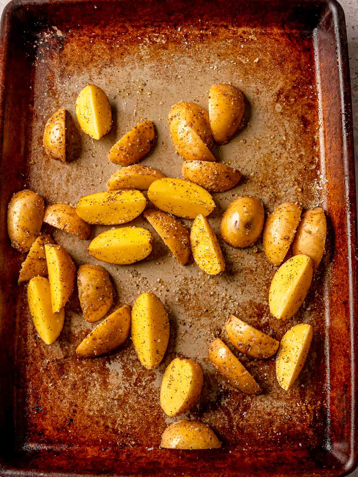 Quartered baby potatoes seasoned with oil, salt, and pepper on a sheet pan.