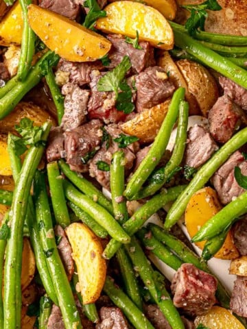 Sheet pan steak bites with roasted potatoes, green beans, garlic-butter sauce, and fresh parsley.