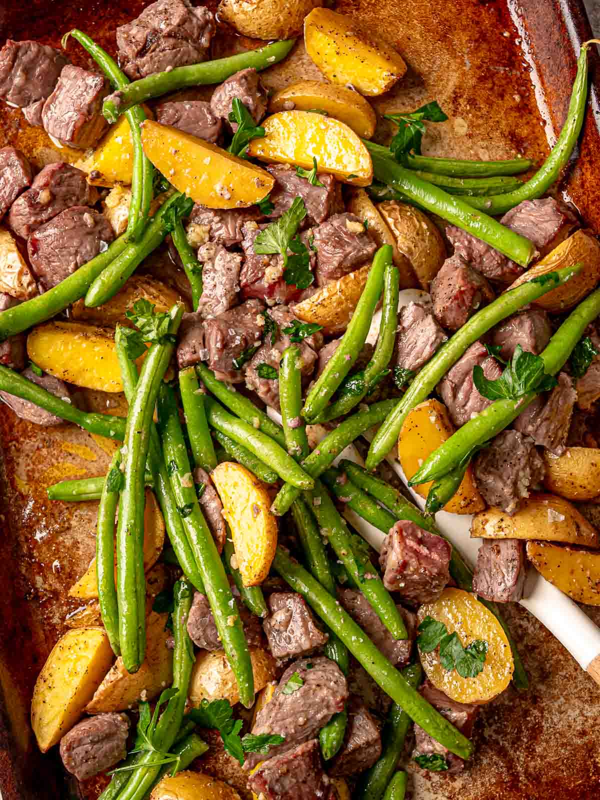 Garlic butter steak bites, potatoes, and green beans roasted together and topped with parsley.