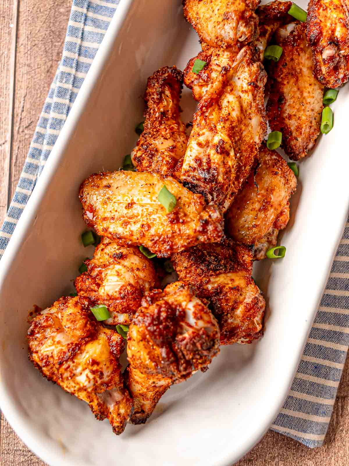 Crispy baked chicken wings served in a white dish and garnished with sliced green onions.