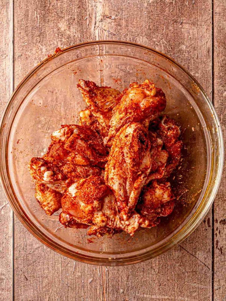 Raw chicken wings coated in seasoning in a glass mixing bowl.