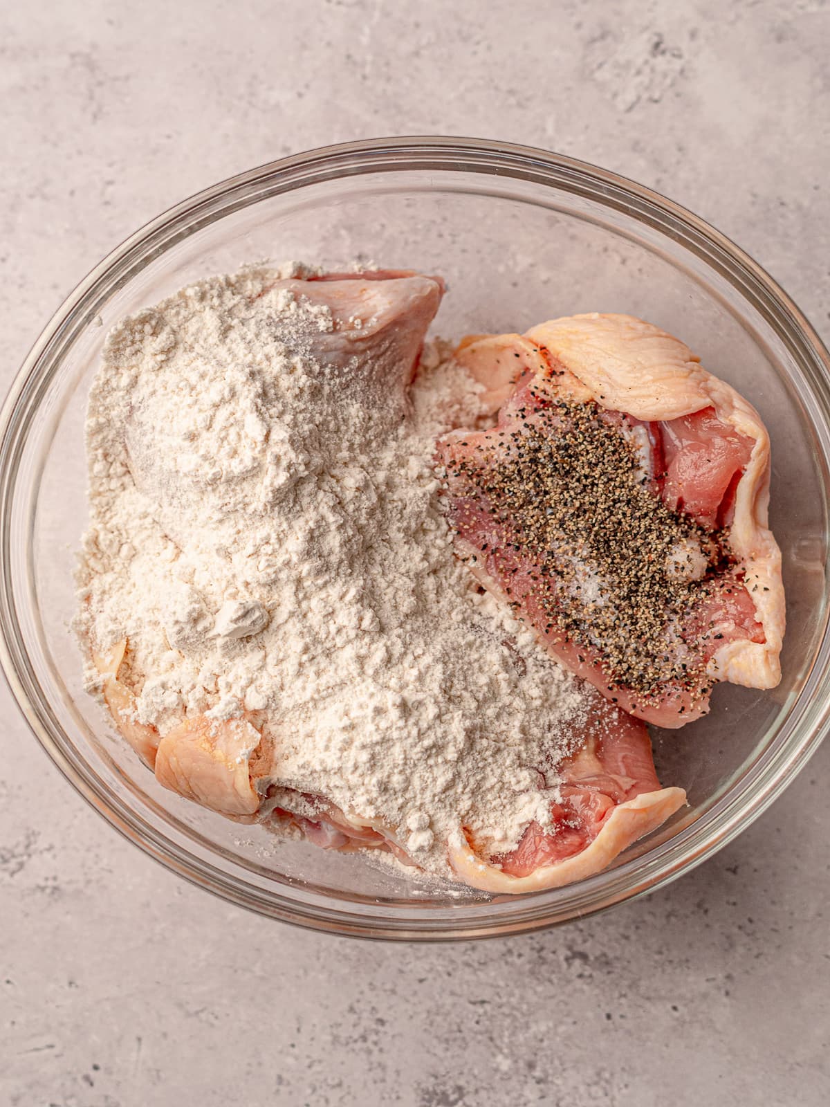 Chicken thighs in a bowl with flour, salt and pepper.