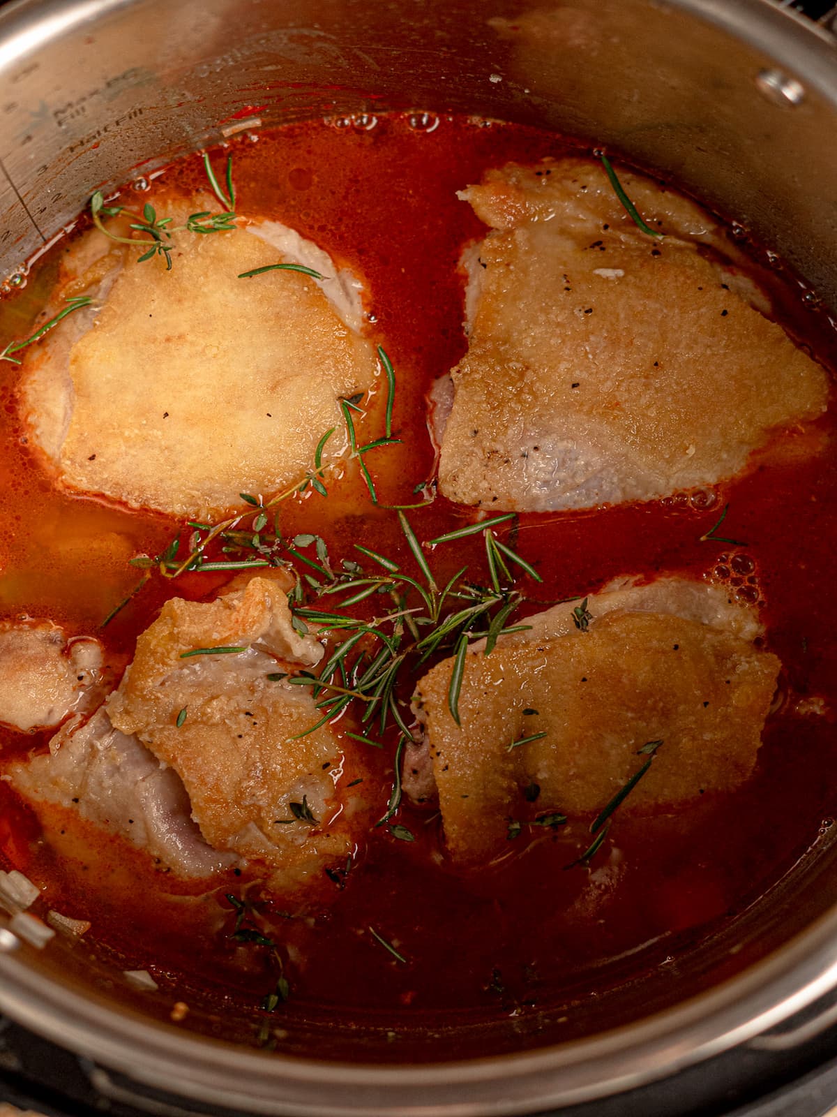 Chicken thighs simmering in a tomato broth.