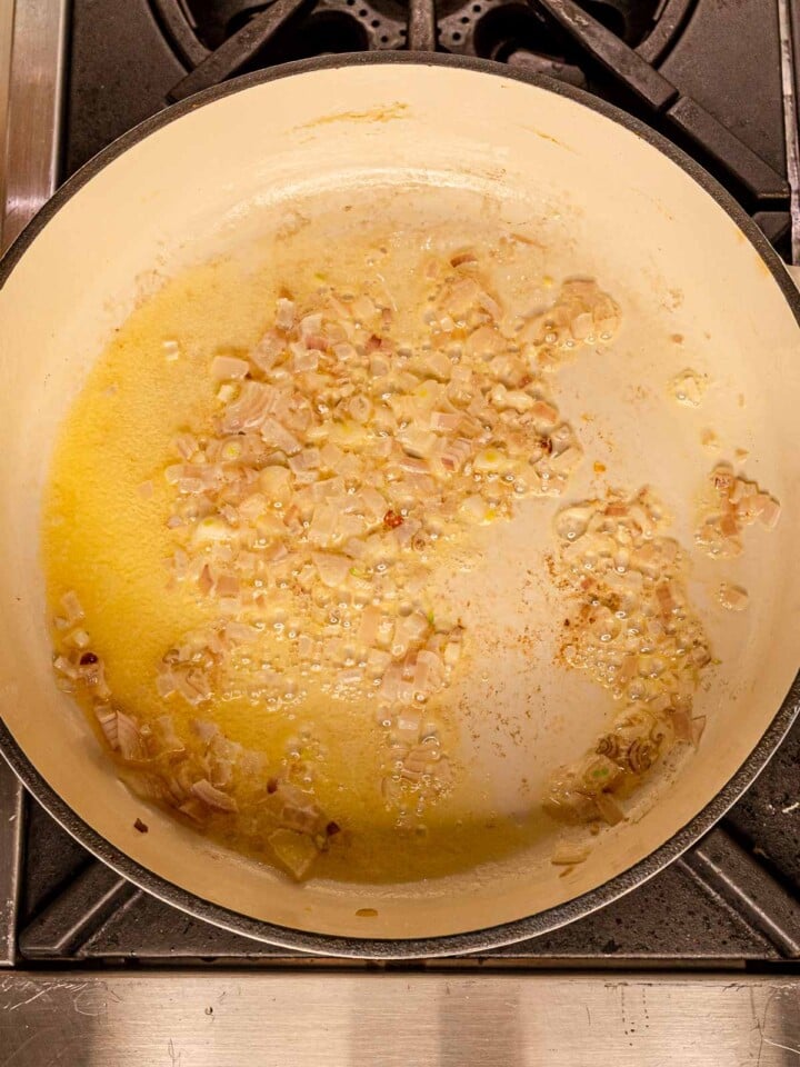 Shallots gently sautéing in butter in a light-colored pan on the stovetop.