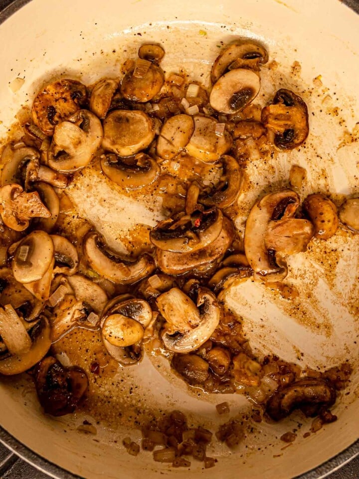 Sliced mushrooms cooking with shallots until golden and lightly caramelized.
