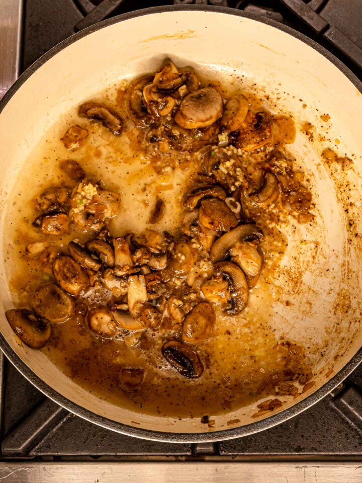 Mushrooms simmering in the pan with pan juices and aromatics.