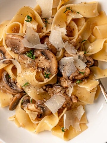 Creamy mushroom pasta plated with Parmesan shavings and cracked black pepper.