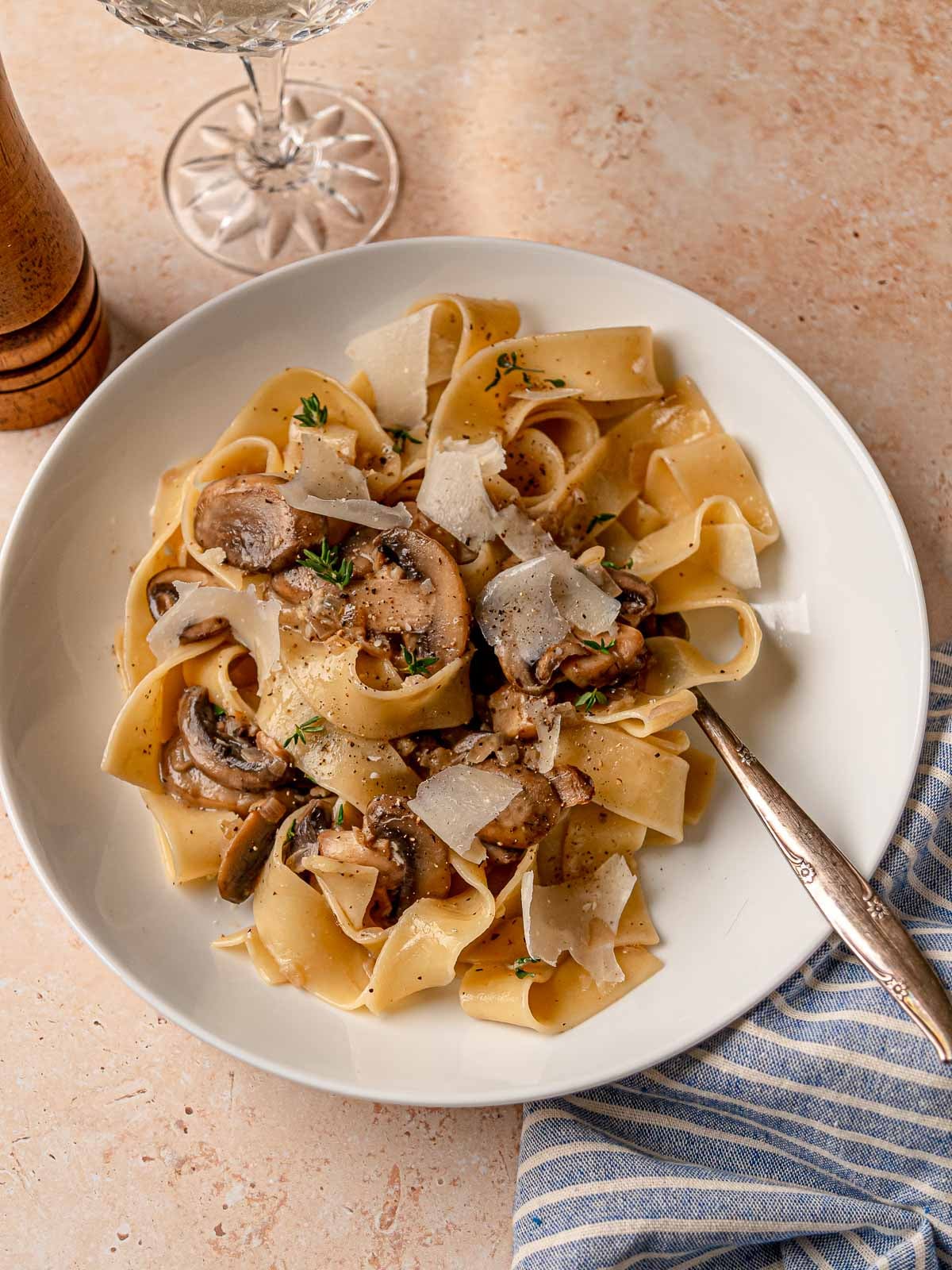 Creamy mushroom pasta served in a white bowl with shaved Parmesan and fresh thyme.