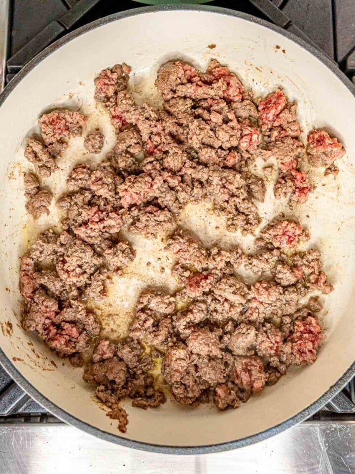 Ground beef browning in a wide skillet until mostly cooked through.