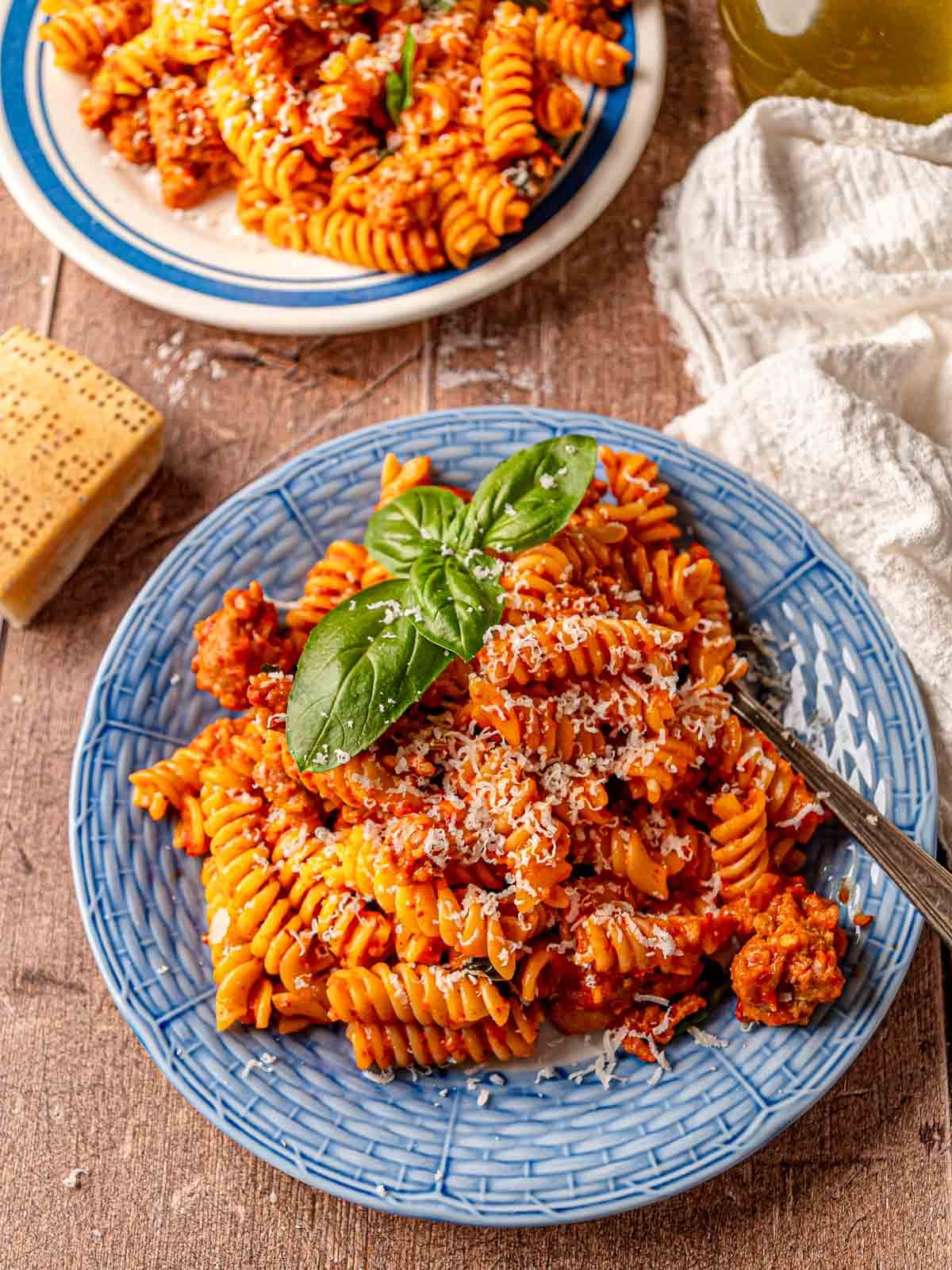 Roasted red pepper pasta with sausage served on a blue plate.