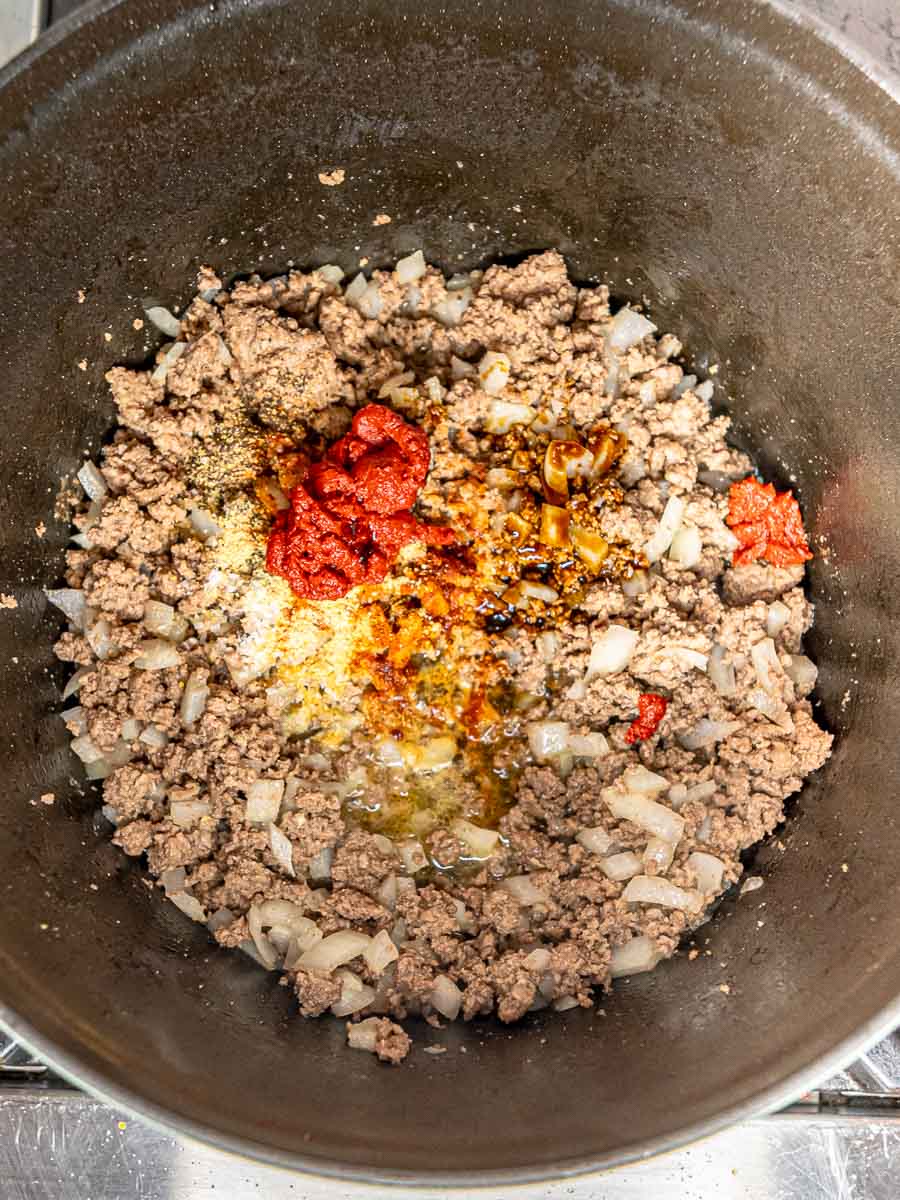 Minced garlic, tomato paste, Worcestershire sauce, and spices added to the skillet with browned beef and onions.