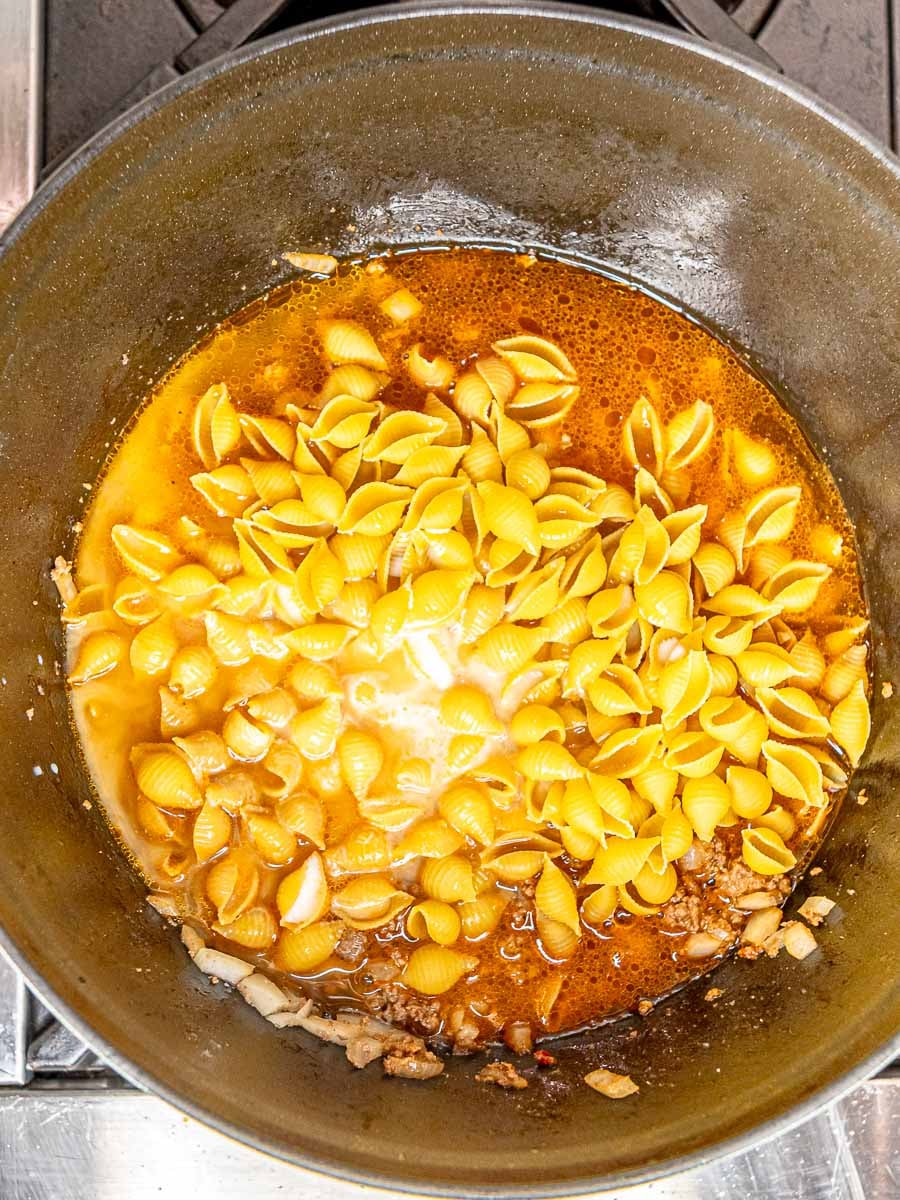 Medium shell pasta and beef broth added to the skillet with the seasoned beef mixture.
