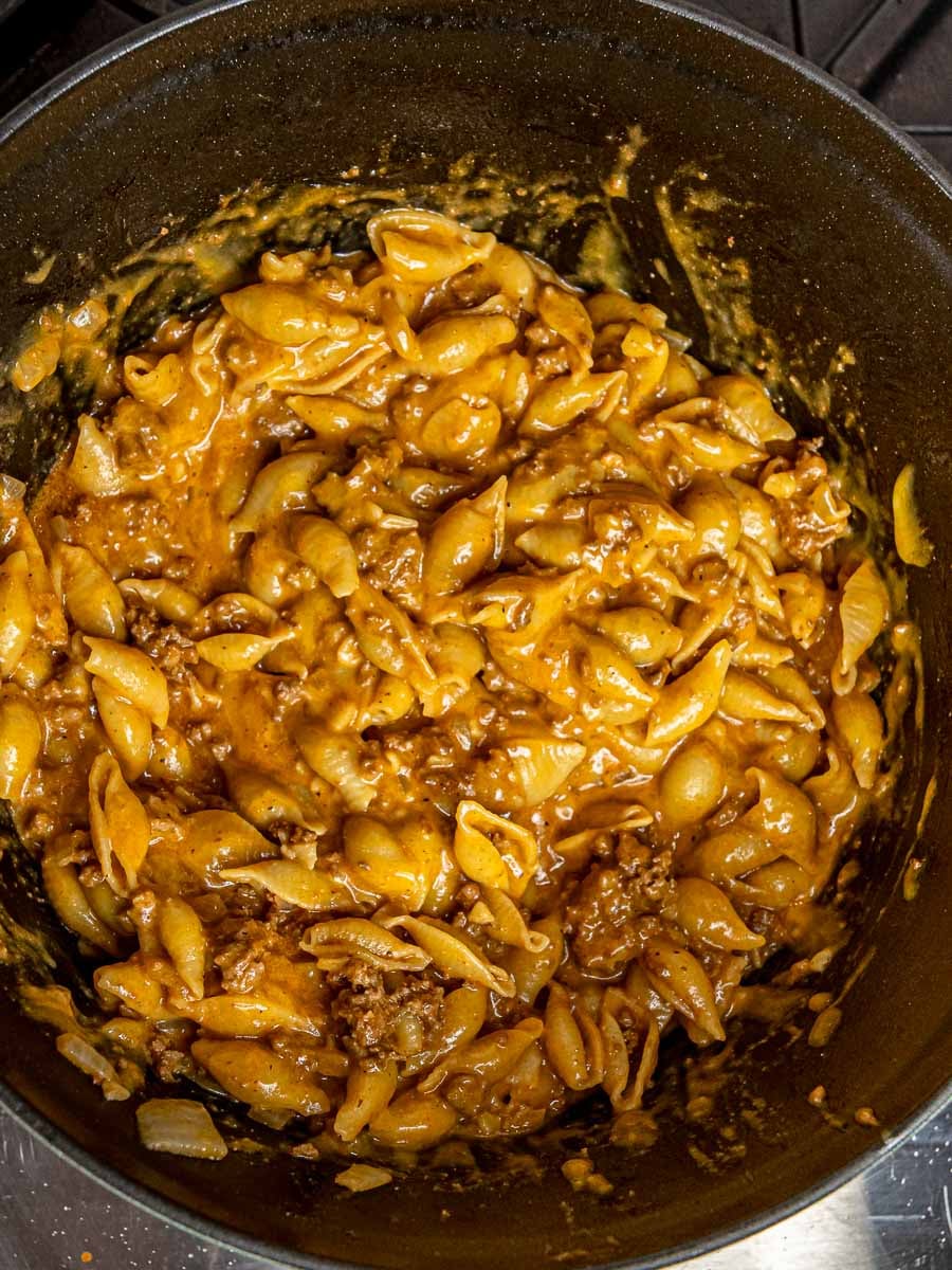 Cooked shell pasta fully coated in a glossy cheeseburger sauce in the skillet.
