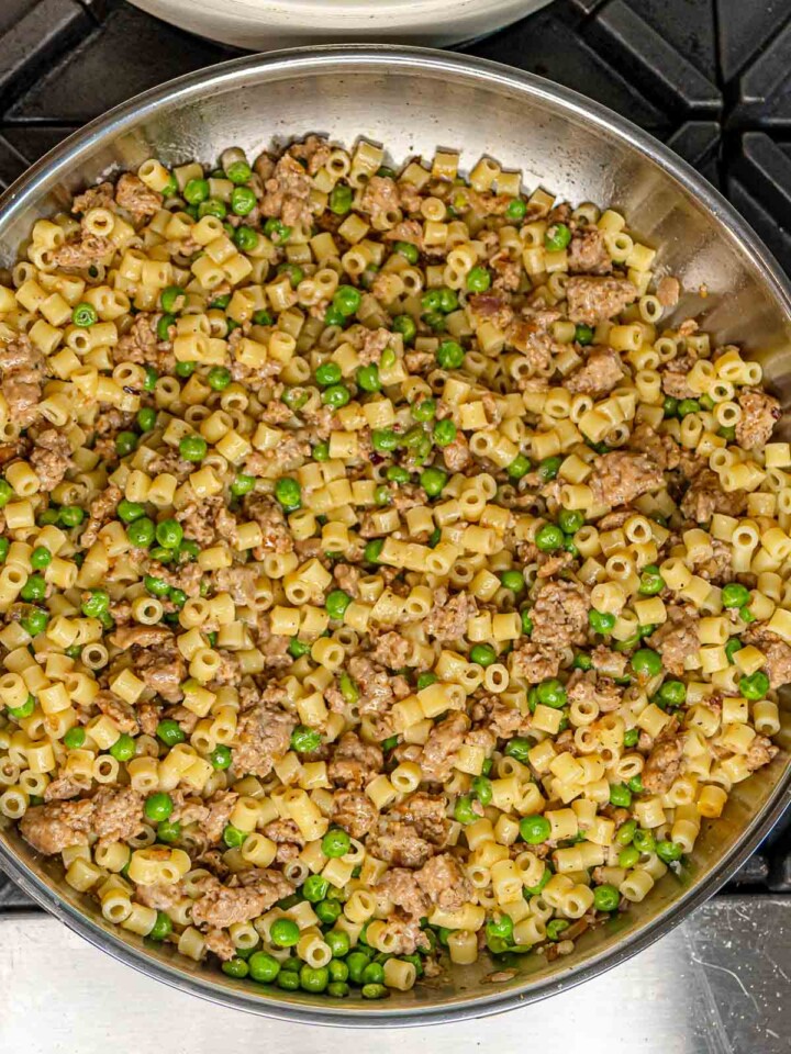 Ditalini pasta fully tossed with crumbled sausage and peas in a stainless steel skillet.