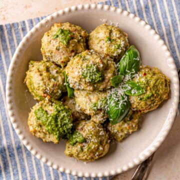 Pesto chicken meatballs garnished with Parmesan cheese and fresh basil leaves on a white plate.