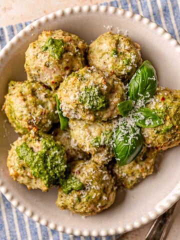 Pesto chicken meatballs garnished with Parmesan cheese and fresh basil leaves on a white plate.
