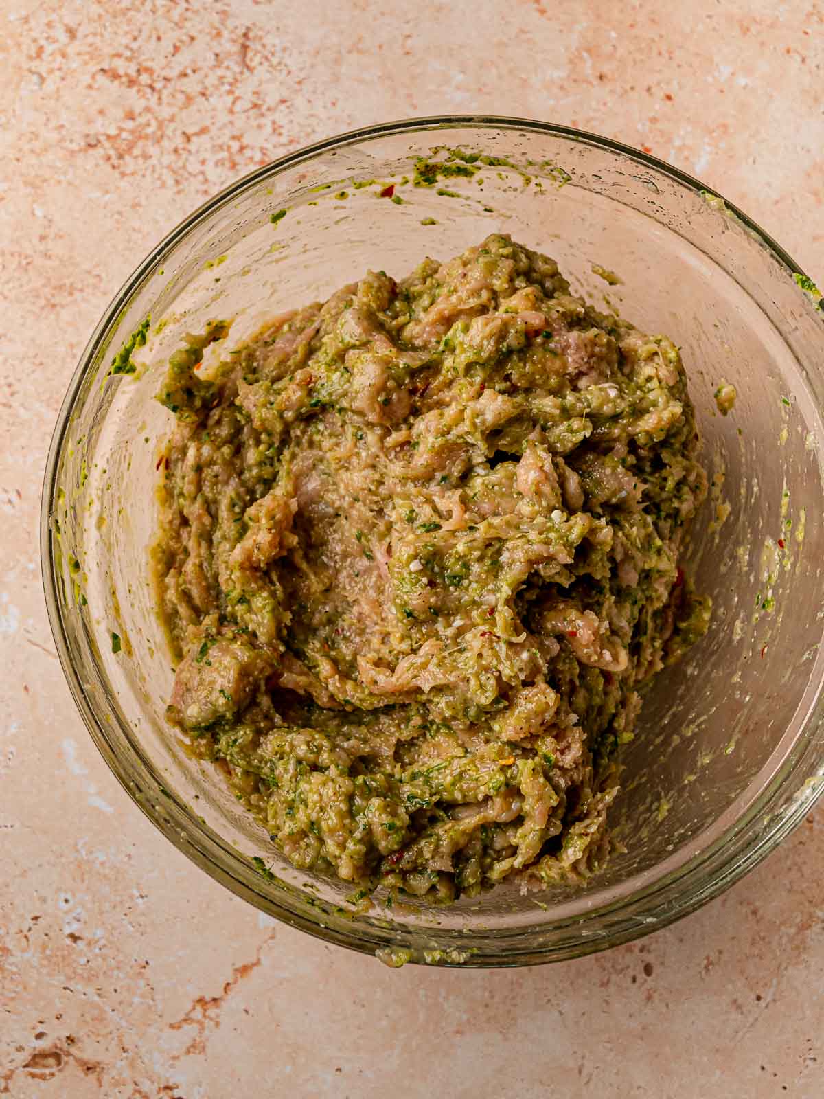 Mixed pesto chicken meatball mixture in a glass bowl showing green-speckled raw ground chicken combined with all ingredients.